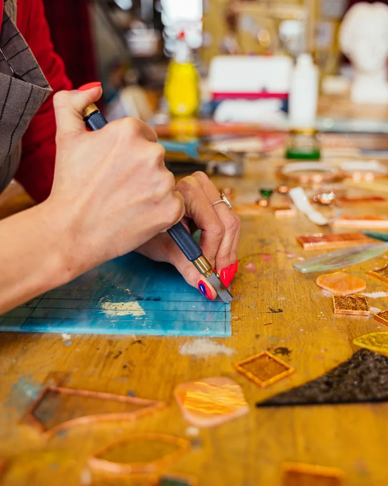 Manos cortando y ajustando una pieza de vidrio de color sobre una mesa de taller de vidriera